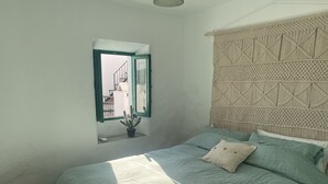 Un dormitorio con cama, ventana con vistas a edificios y un cabecero de macramé.
