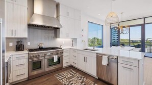 A modern kitchen with white cabinetry, a stainless steel range, and a large window offering a view. - Gulf Views - Rooftop Deck- Private Poolside Cabana (Santa Rosa Beach)