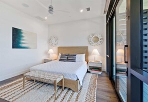 Un dormitorio moderno con una cama grande, mesitas de noche, un banco y vistas a través de un ventanal.