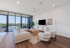 Un moderno salón con sofá, sillones, una mesa de centro, televisor y un amplio ventanal con vistas a un balcón.