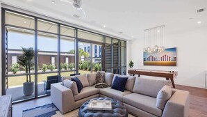 A modern living room with a sectional sofa, a round ottoman, and a large window offering a view of the outdoors. - Gulf Views - Rooftop Deck- Private Poolside Cabana (Santa Rosa Beach)