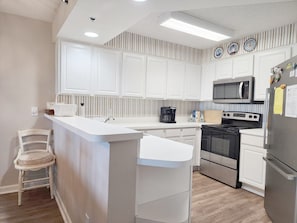 A modern kitchen with white cabinetry, a central island, a microwave, a stove, and a refrigerator. - Warwick 203 Oceanfront - Great views of Ocean & Pool, Clubhouse Access (Pawleys Island)