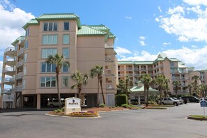 A multi-story hotel with a green roof, multiple balconies, and a parking lot with several cars. - Warwick 203 Oceanfront - Great views of Ocean & Pool, Clubhouse Access (Pawleys Island)