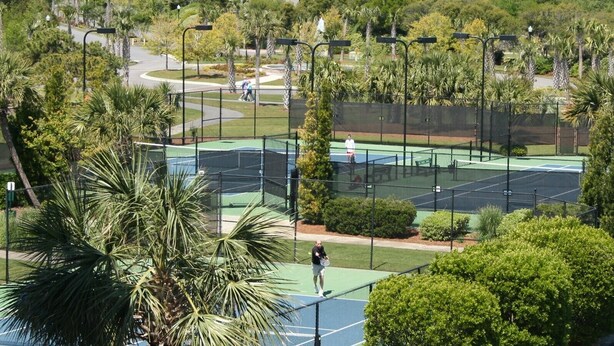 Ein Tennisplatz, umgeben von üppiger Vegetation und Wohnhäusern.