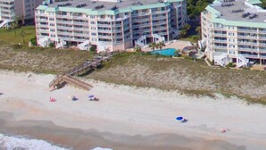 Ein Hotel direkt am Strand mit mehreren Balkonen, einem Poolbereich und einer Promenade, die zum Strand führt.