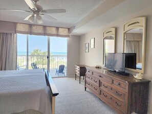 Ein Hotelzimmer mit Bett, Schminktisch, Fernseher und einem Balkon mit Blick auf den Strand.