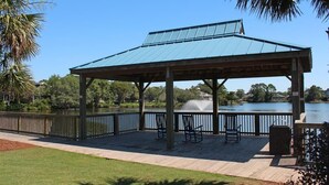 Ein überdachter Pavillon mit Metalldach, der auf einen See blickt, umgeben von einer Holzterrasse und einem schwarzen Geländer.