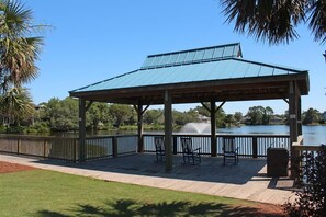 A covered pavilion with a metal roof overlooking a lake, surrounded by a wooden deck and a black railing. - Warwick 203 Oceanfront - Great views of Ocean & Pool, Clubhouse Access (Pawleys Island)