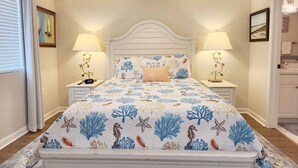 Une chambre à coucher comprenant un lit, deux tables de chevet avec des lampes, un ventilateur de plafond et une fenêtre avec des rideaux.