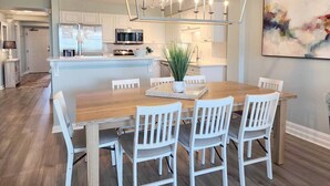 Een moderne keuken met witte kasten, een centraal eiland en een eetgedeelte met een houten tafel en witte stoelen.