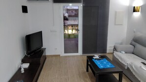 Ein Wohnzimmer mit Flachbildfernseher, einer Couch, einem Couchtisch und einer Glastür, die auf einen Balkon führt.
