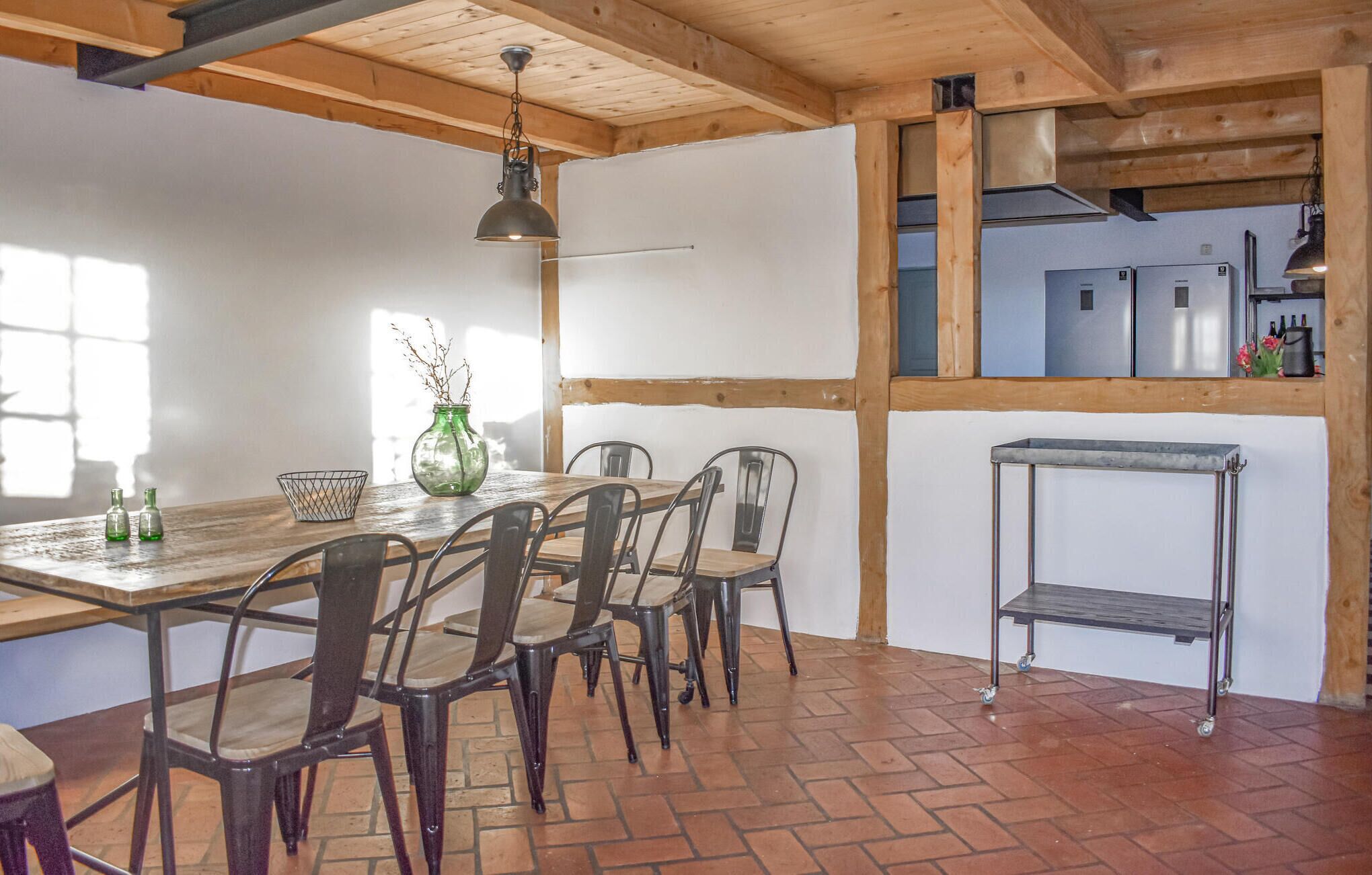 Un espace repas comprenant une table et des chaises en bois, un luminaire suspendu, ainsi qu’un coin cuisine avec des placards et un réfrigérateur.