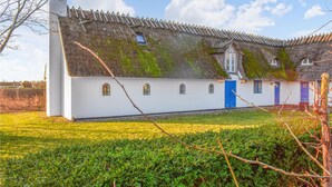 Een traditioneel huis met rieten dak, witte muren en meerdere ramen.