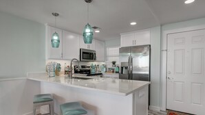 A modern kitchen with white cabinetry, stainless steel appliances, and teal bar stools. - Steps To The Sea | Penthouse with Ocean Views (Port Aransas)