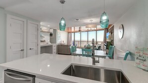 A modern kitchen with a large island, stainless steel sink, and teal chairs. - Steps To The Sea | Penthouse with Ocean Views (Port Aransas)