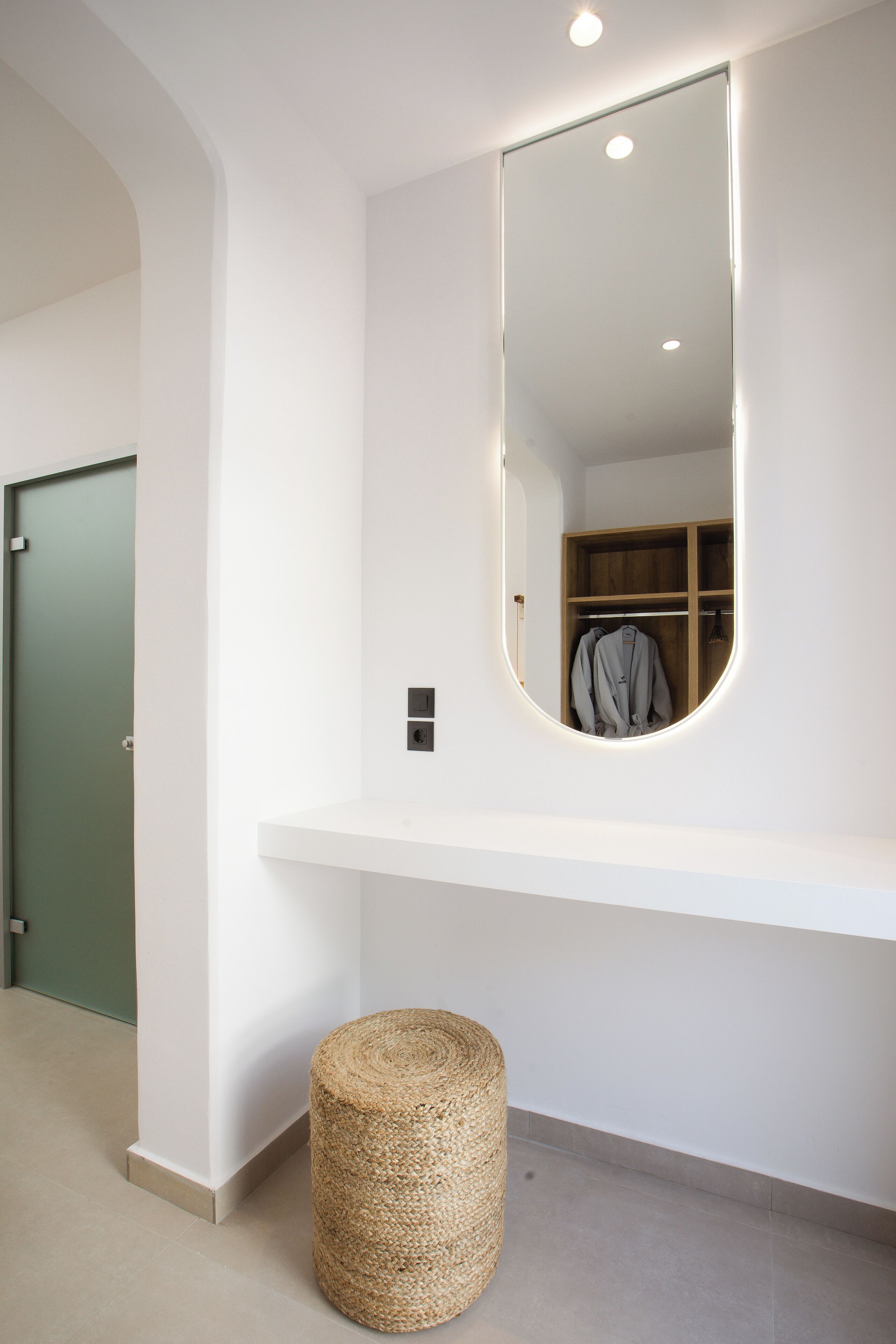 A modern bathroom with a large mirror, a wooden vanity, and a round wicker stool.