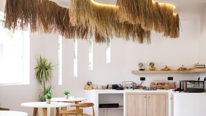 A modern kitchen with white cabinetry, a wooden countertop, and a hanging thatch ceiling. - Stay Helios - Aparts & Pool Suites (Rhodes)