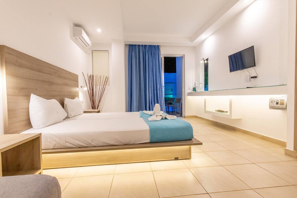 A modern hotel room with a bed, bedside table, TV, and a bathroom visible through a door.