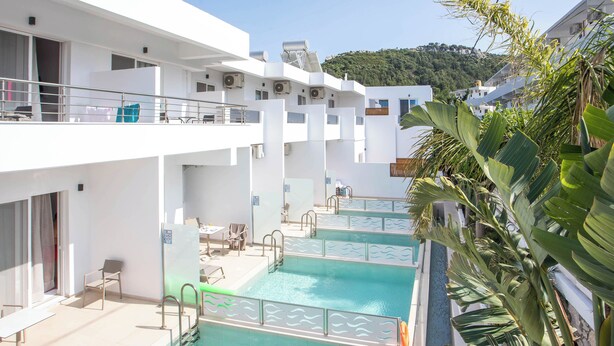 A pool area with multiple swimming pools, lounge chairs, and a view of a hillside. - Stay Helios - Aparts & Pool Suites (Rhodes)