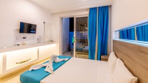 A modern hotel room with a bed, a bedside table, a TV, and a sliding glass door leading to a balcony. - Stay Helios - Aparts & Pool Suites (Rhodes)