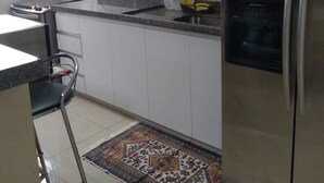 Una cocina con gabinetes blancos, un refrigerador de acero inoxidable, una estufa a gas y un tapete estampado.