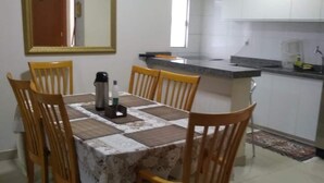 Un comedor con una mesa dispuesta para seis personas, rodeada de sillas de madera. Hay una cafetera y una botella sobre la mesa.