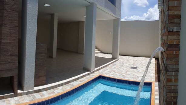 Una piscina con una fuente de agua azul cristalina, rodeada por un solárium con baldosas y un muro de ladrillo.