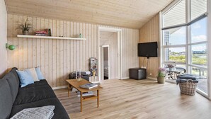 A spacious living room with a wooden ceiling and floor, a large window offering a view, a flat-screen TV mounted on the wall, and a cozy seating area with a sofa and a coffee table. - Pet friendly home in Hejls with WiFi (Hejls)