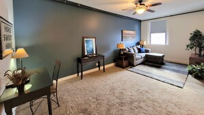 A living room with a dark blue wall, a ceiling fan, a sofa, a coffee table, and a dining table with chairs.
