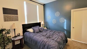 A bedroom with a bed, a nightstand, a lamp, a ceiling fan, and decorative wall art.