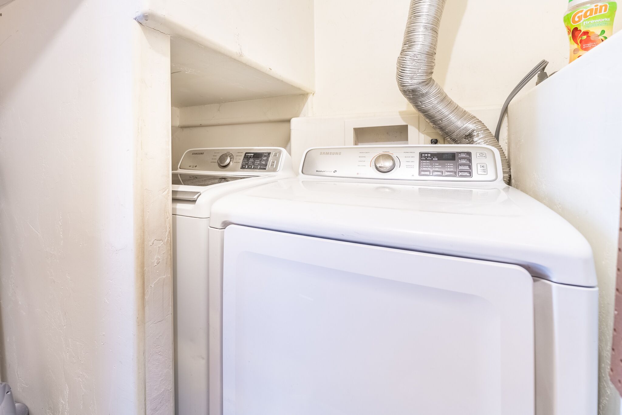 A front-loading washer and dryer in a laundry room with a visible vent hose.