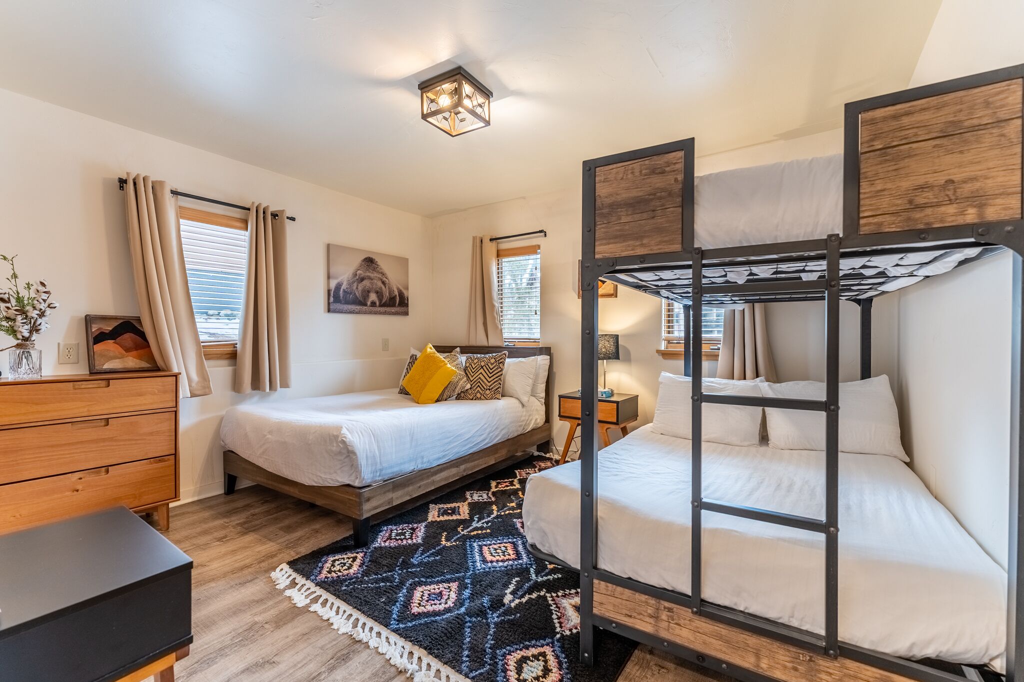 Een slaapkamer met een stapelbed, een enkel bed, een houten dressoir, een kamerbreed tapijt met een patroon en een plafondlamp.