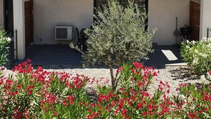 A two-story building with a tiled roof, a covered entrance, and a small garden with red flowers. - Beautiful 4-6 person gîte in the center of Vallon Pont d'Arc (Vallon-Pont-d'Arc)