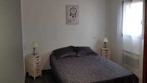 A bedroom with a bed, a bedside table with a lamp, a wall-mounted dreamcatcher, and a window with blinds. - Beautiful 4-6 person gîte in the center of Vallon Pont d'Arc (Vallon-Pont-d'Arc)