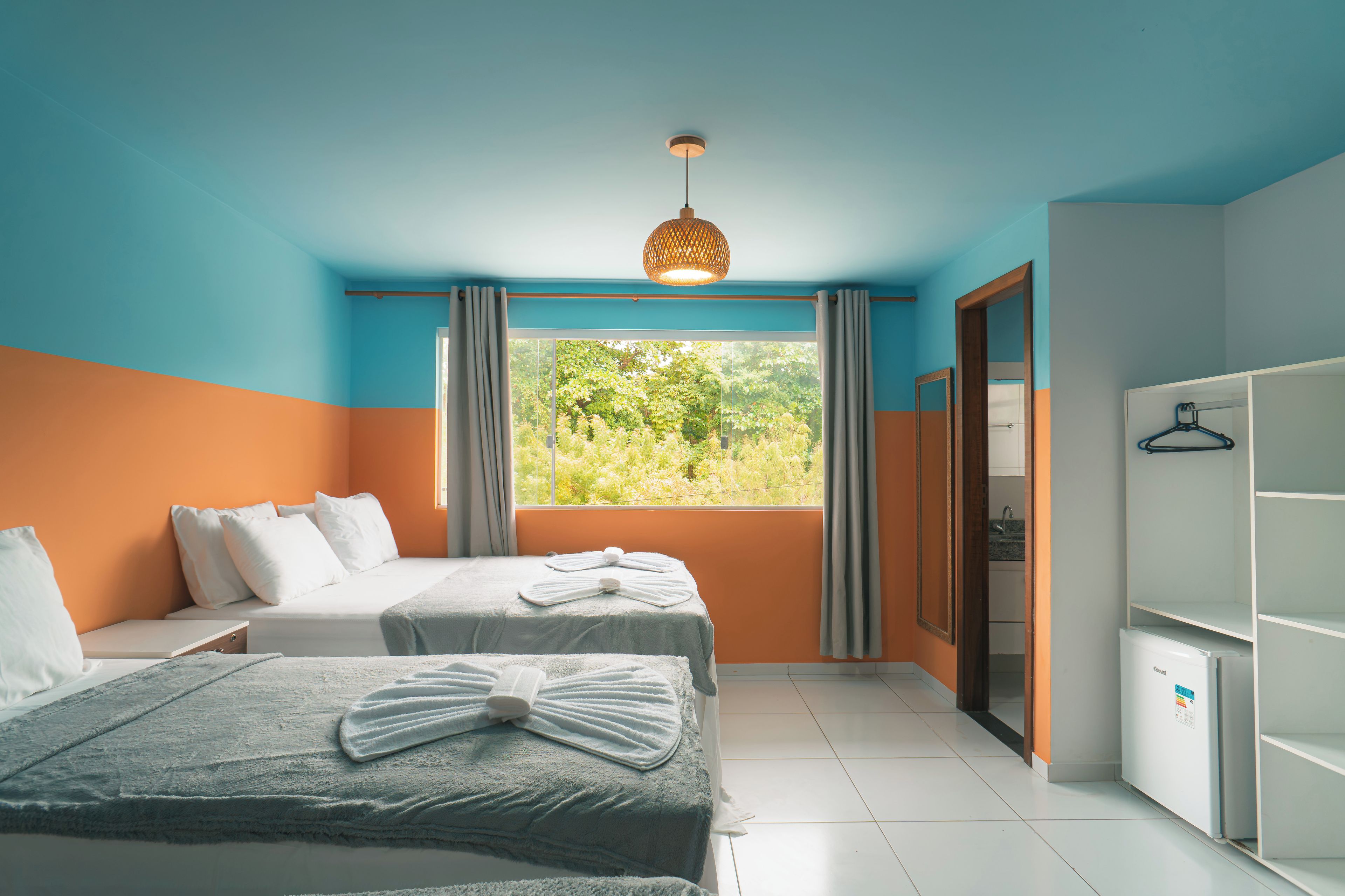 Une chambre avec deux lits, une armoire et une fenêtre donnant sur un paysage verdoyant.