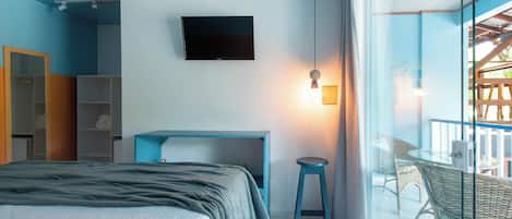 Un dormitorio con cama, escritorio, silla, televisor y balcón con mobiliario de mimbre.