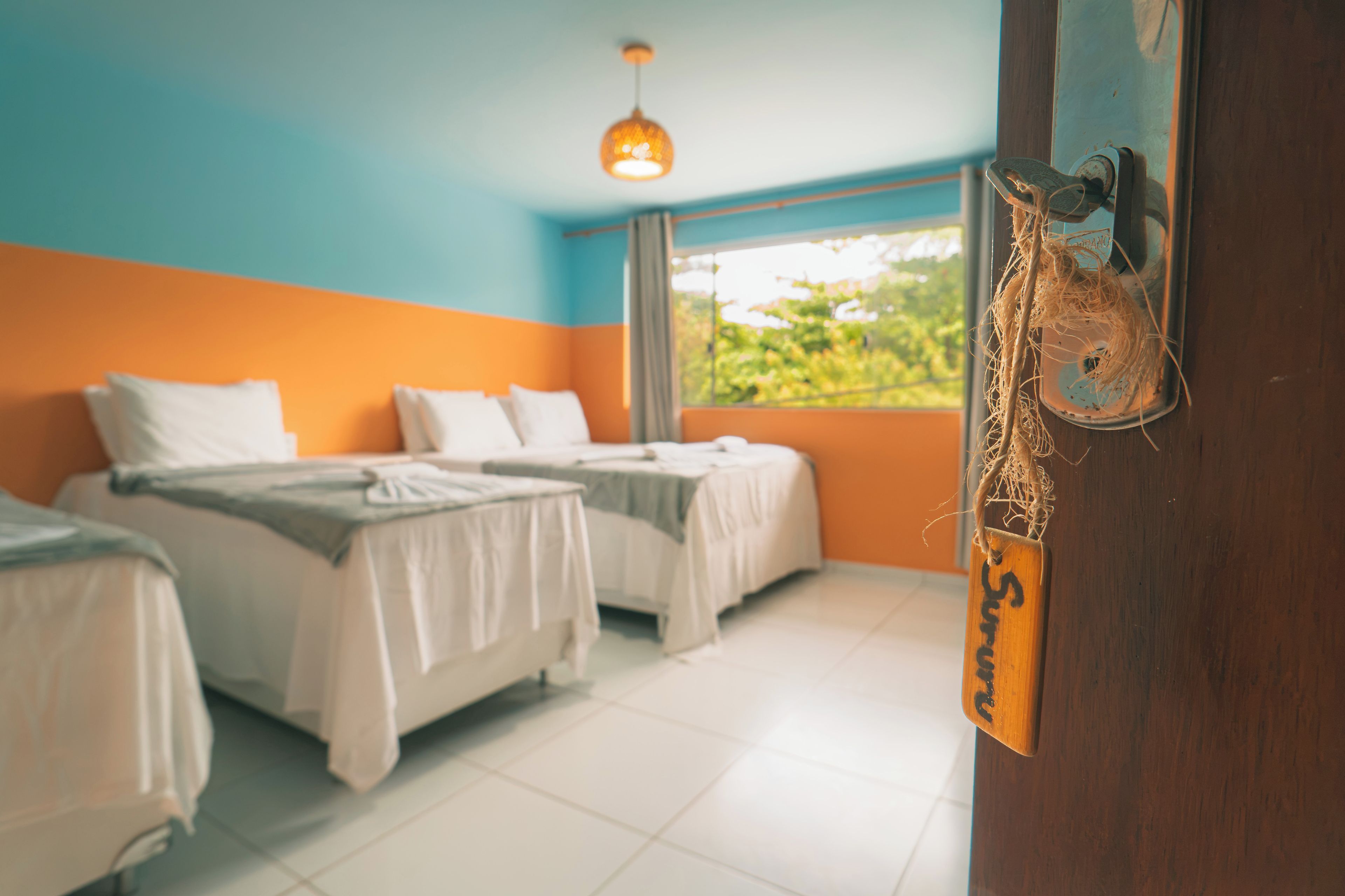 Habitación de hotel con dos camas, una ventana con vistas a follaje y un adorno colgante.