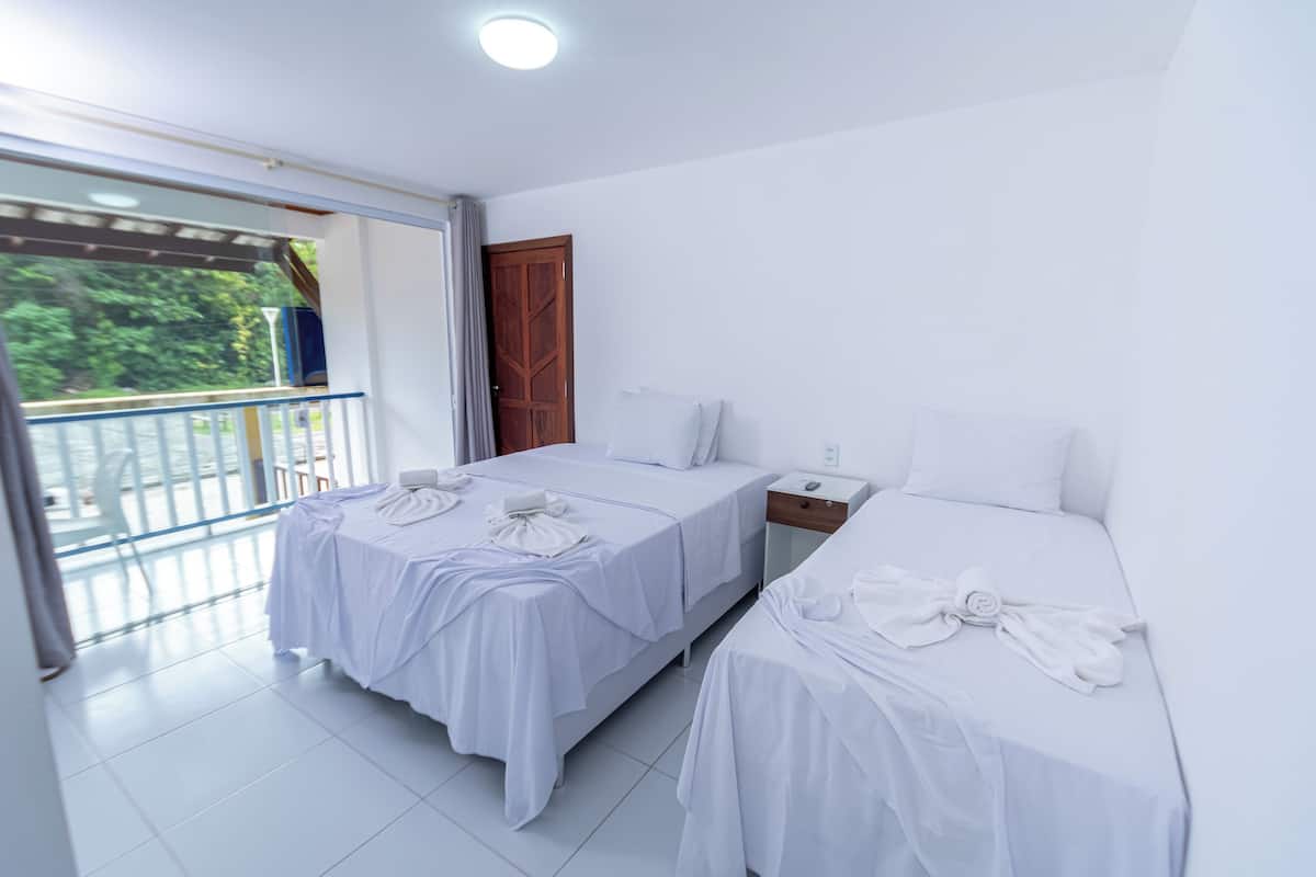 A hotel room with two beds, a balcony, and a view of greenery.