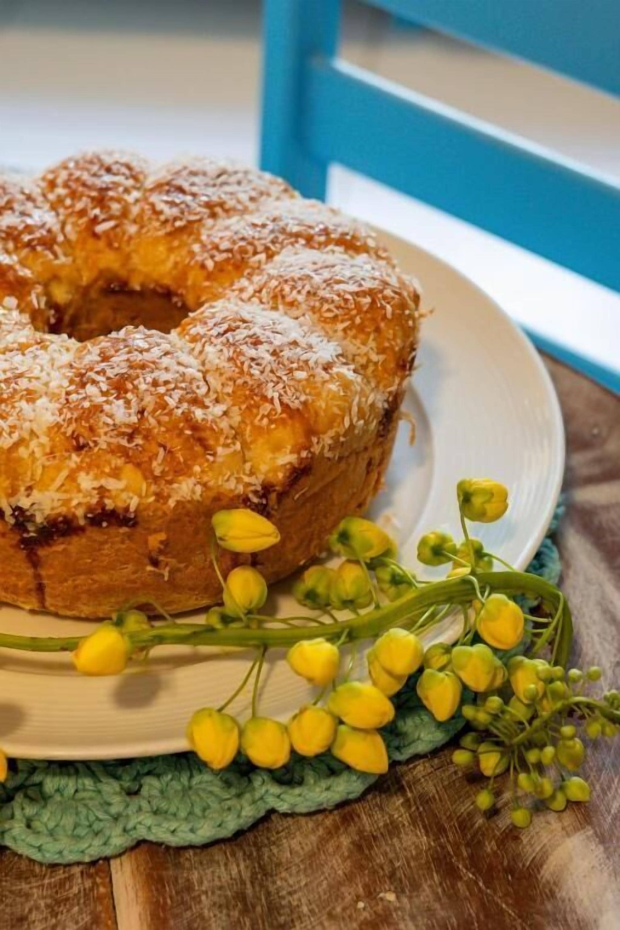 A bundt cake on a plate with a green cloth underneath, accompanied by yellow flowers.