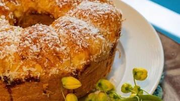 A bundt cake on a plate with a green cloth underneath, accompanied by yellow flowers.