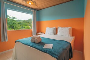 A bedroom with a bed, a nightstand, a window with curtains, and a view of greenery outside. - Hotel do Pescador (Cairu)