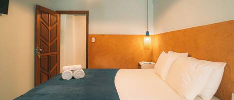 A hotel room with a bed, a nightstand, a wall-mounted lamp, and a door.
