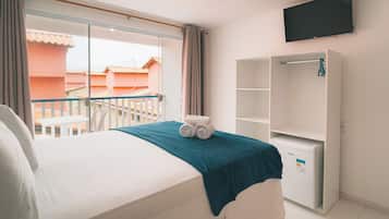 Habitación de hotel con cama, televisor montado en la pared, armario y balcón con vistas a edificios.