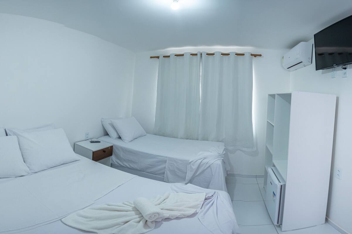 A hotel room with two beds, a TV, an air conditioning unit, and a wardrobe.
