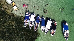 An aerial view of a beach with several boats docked in a row, surrounded by clear shallow water and some vegetation. - Hotel do Pescador (Cairu)
