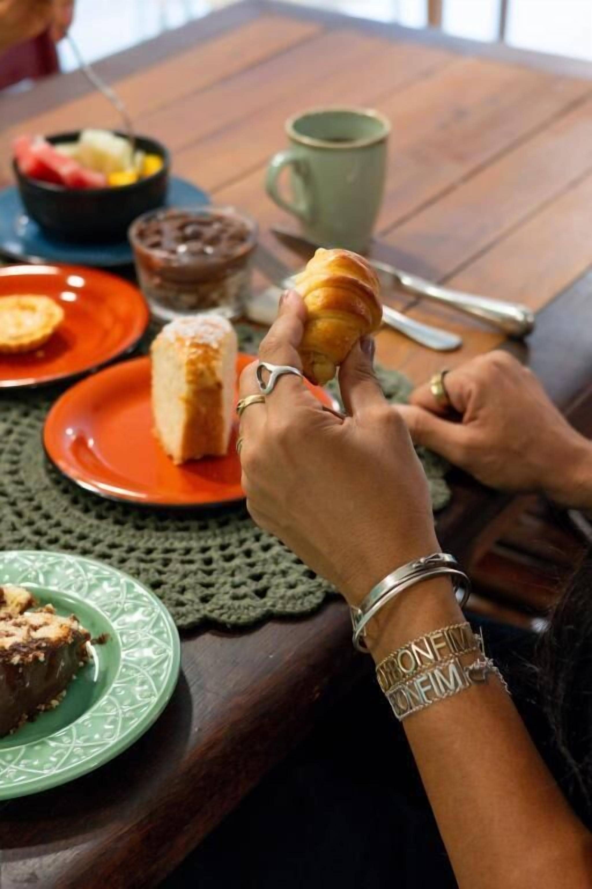 Una mesa de comedor con un plato de comida, una taza y una persona sosteniendo un pastel.