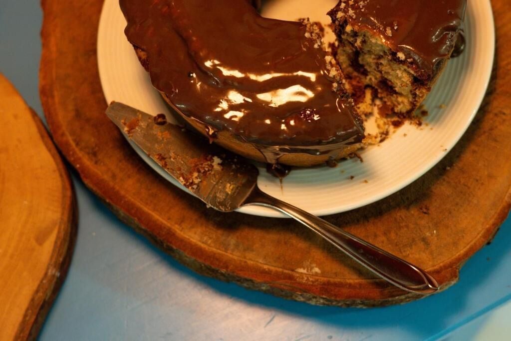 Un pastel cubierto de chocolate, con una porción cortada, sobre un plato blanco, colocado en una tabla de madera.