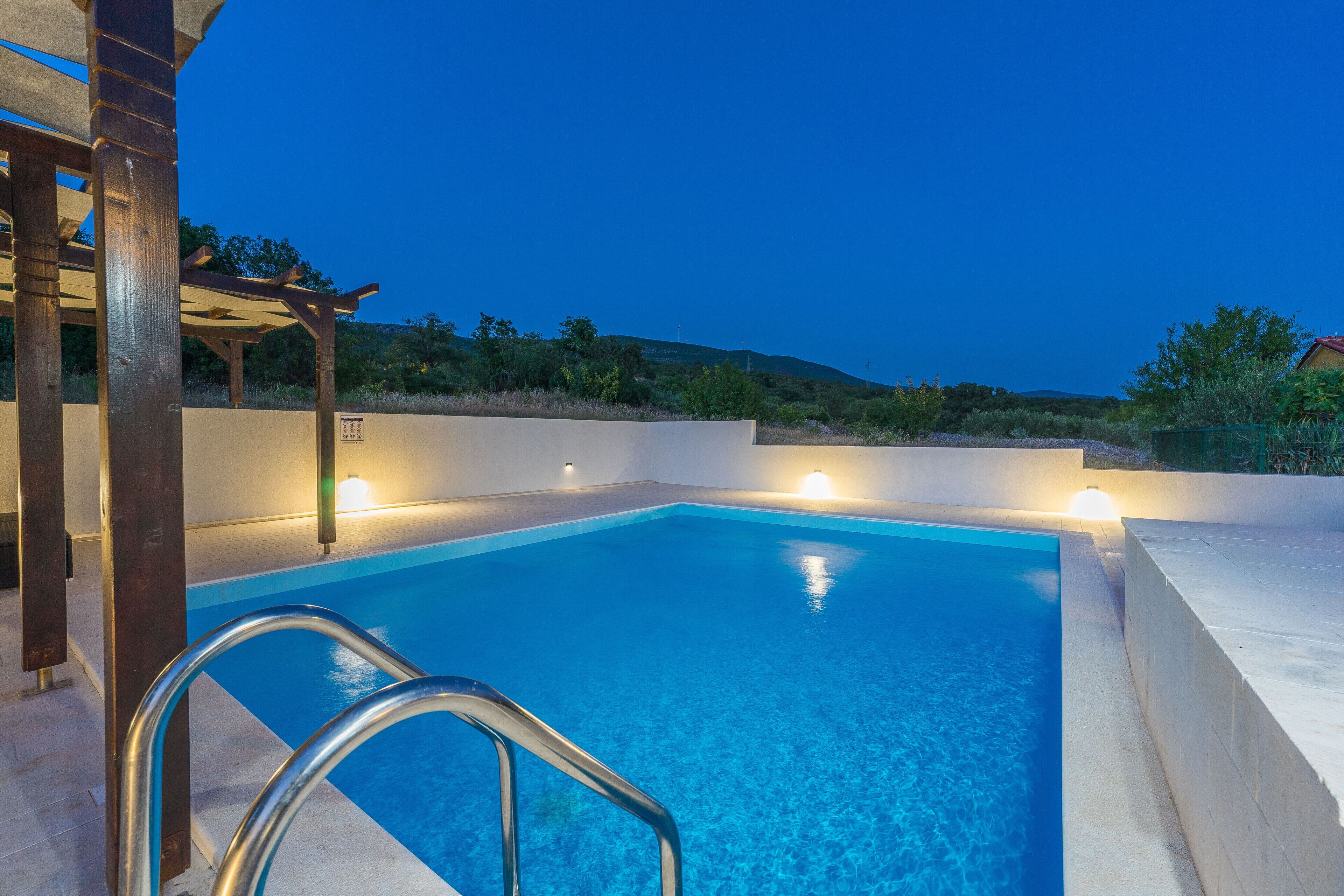 Ein Schwimmbecken mit Metallleiter, umgeben von einer Betonplattform und einer Holzpergola.