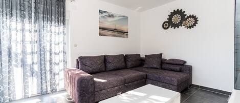 En moderne stue med en hjørnesofa, et hvidt sofabord og et stort vindue med mønstrede gardiner.