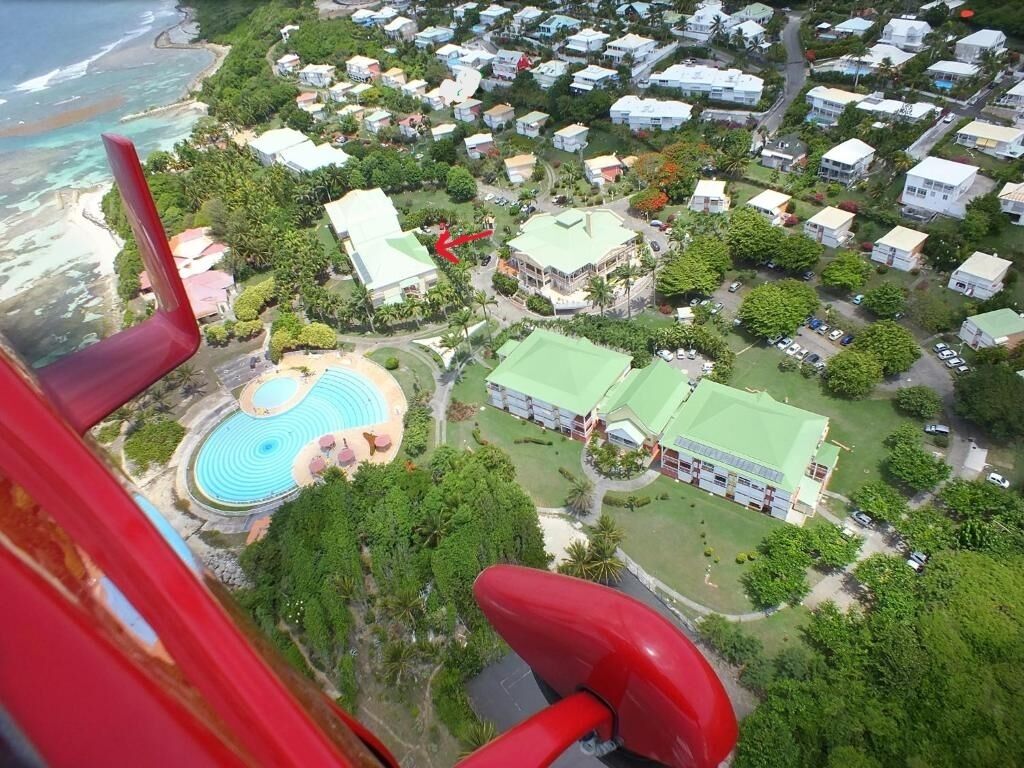 Vista aérea de uma área residencial costeira com casas, uma piscina e um edifício grande com telhado verde.